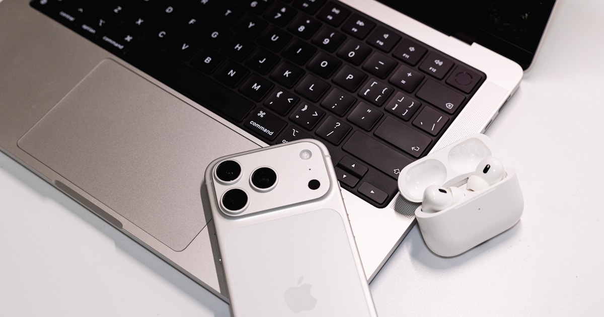 ノートPCとスマートフォン、AirPods Pro風のイヤホンが並んだ在宅ワークのデスク